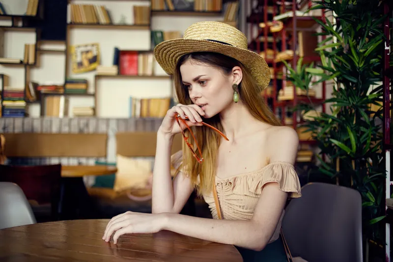 Симпатичная женщина в шляпе сидит за столом с книгами на заднем плане, крупный план