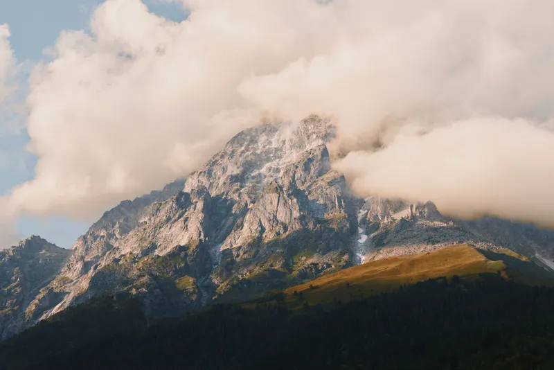 Majestic mountain peak rising above a pine forest, with wispy clouds, rugged rock, and expansive alpine landscape highlighting nature, scale, and solitude and calm mood.