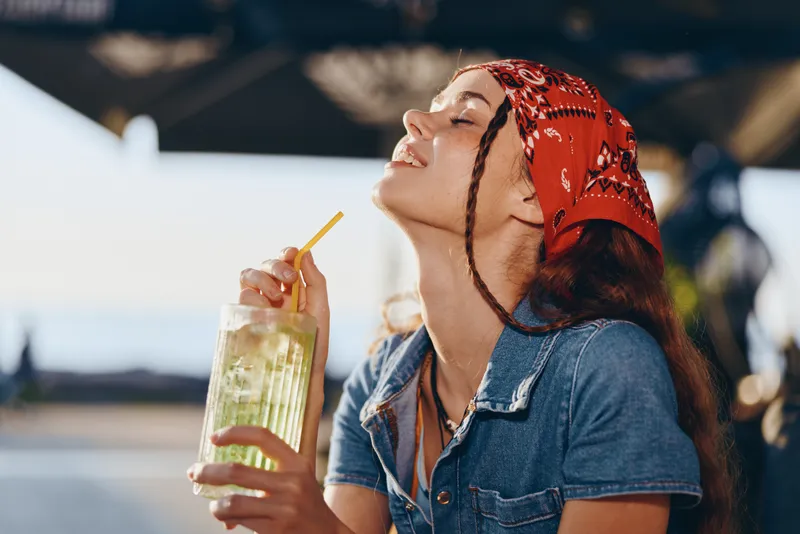 lifestyle woman in modern boho-western denim street style enjoying refreshing drink, film color, casual summer moment filled with joy and relaxation outdoors