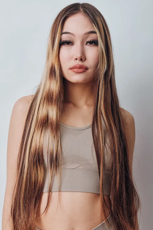 Young woman with long straight hair and natural makeup posing in beige crop top against light background for beauty portrait and fashion style.