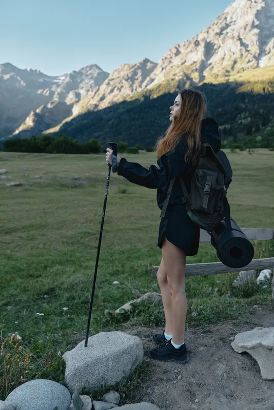 A young hiker stands on a rugged trail with a trekking pole, gazing toward distant peaks, wearing a backpack and outdoor gear, capturing a moment of adventure and exploration.