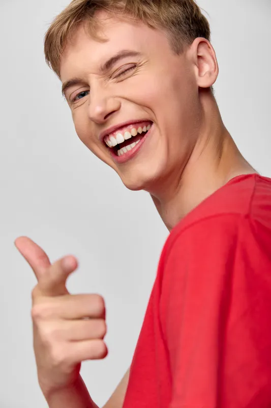 Smiling young man in a casual red shirt making a pointing gesture, conveying happiness, fun and friendly expression for lifestyle, advertising and marketing visuals