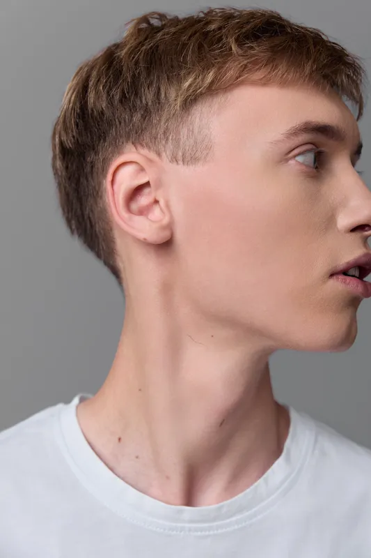 Profile view of a young man in a white shirt, thoughtful expression, clean studio lighting, neutral gray backdrop, contemporary casual style, suitable for lifestyle, fashion, or creative projects in