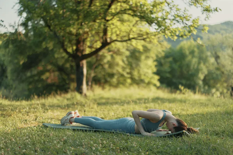 Young woman practicing yoga outdoors in a serene natural setting, showcasing flexibility and tranquility while wearing comfortable activewear on a sunny day