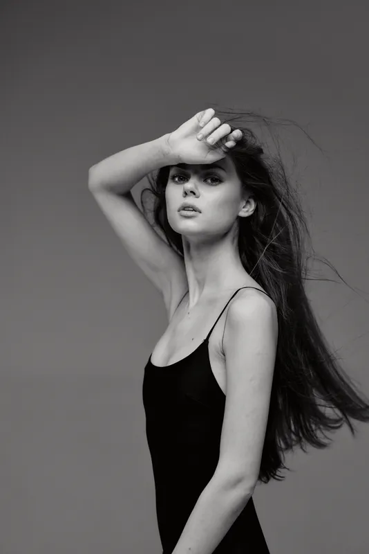 Black and white portrait of a young woman with long hair wearing a black dress with a pensive expression.
