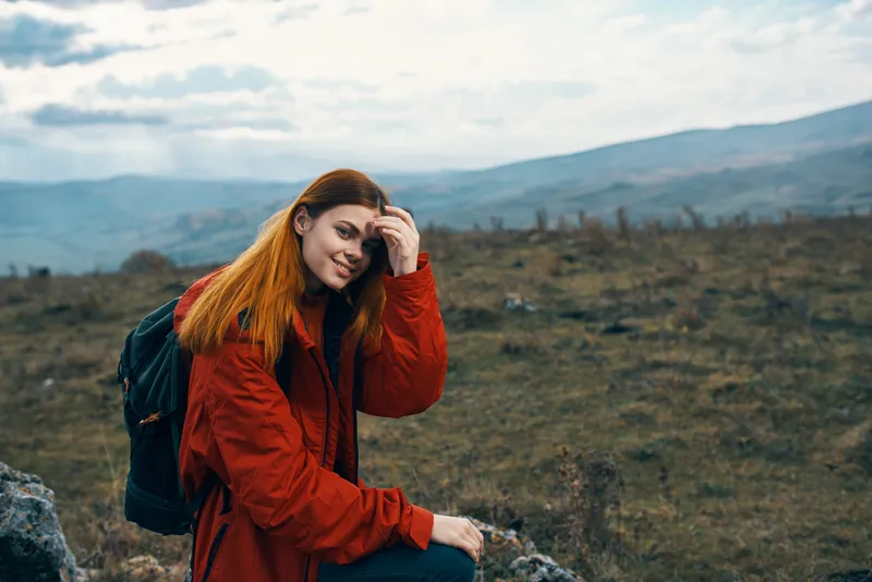 Счастливая женщина-туристка присела отдохнуть на лугу в горах, на природе