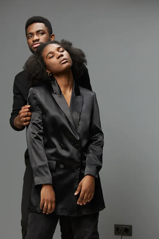 Elegant black couple in stylish outfit embracing against neutral background, showcasing love and confidence in a modern setting