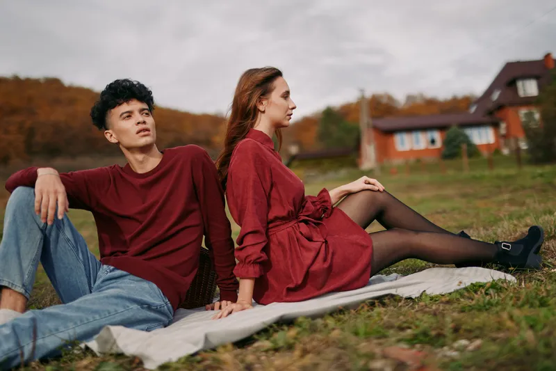 A young couple sits on a blanket in a rural autumn field, sharing a quiet, genuine moment of connection and contemplation that emphasizes natural emotion and visual authenticity.