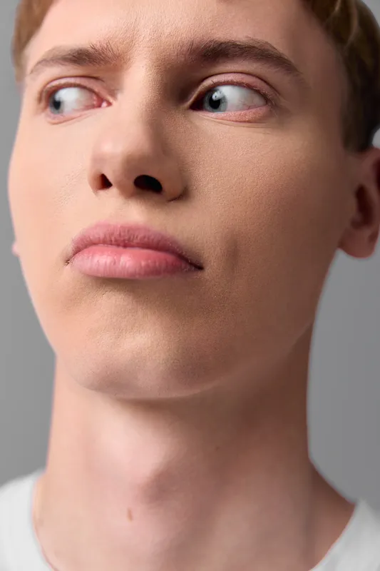 Closeup of a young male with curious expression looking to the side, showcasing smooth skin and defined jawline for exploring doubt, contemplation, focus, and attention in creative projects.