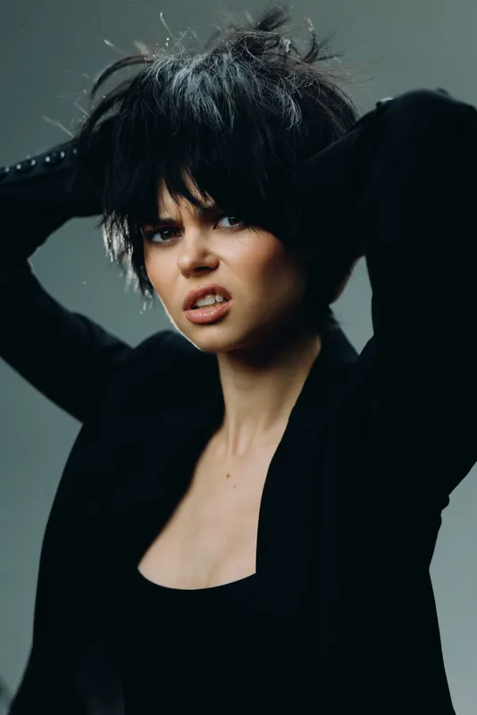 Young woman with short dark hair expressing frustration wearing black clothing in studio light