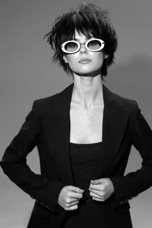 Stylish woman in black blazer with white sunglasses posing confidently in black and white portrait