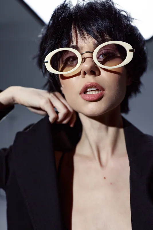 Stylish woman wearing large white sunglasses and black outfit with confident expression in studio lighting