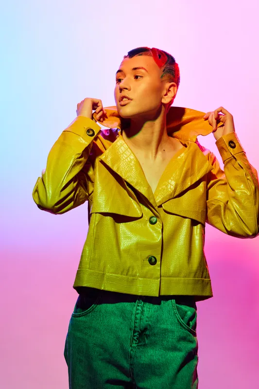 young woman in yellow jacket posing confidently with colorful lighting and vibrant background, expressing bold style and modern fashion attitude