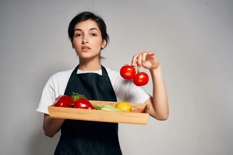 Шеф-повар в черном фартуке на изолированном фоне со свежими овощами и продуктами