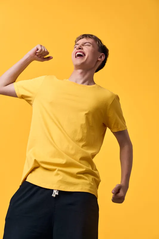 Celebration scene with a young man in a yellow shirt expressing joy and energy against a vivid yellow backdrop, conveying optimism and an upbeat mood