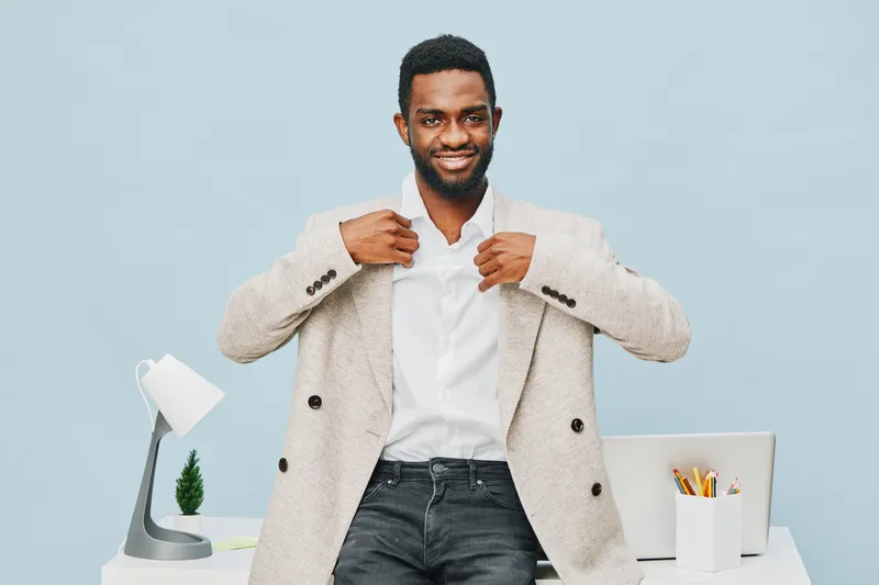 Smiling man adjusting beige blazer in modern office setting. Caucasian male, early 30s, trendy business casual style, confident expression, bright background, professional work environment, concept: b