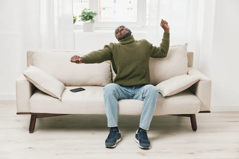 A joyful man in a green sweater relaxing on a couch, expressing happiness and comfort in a bright indoor space