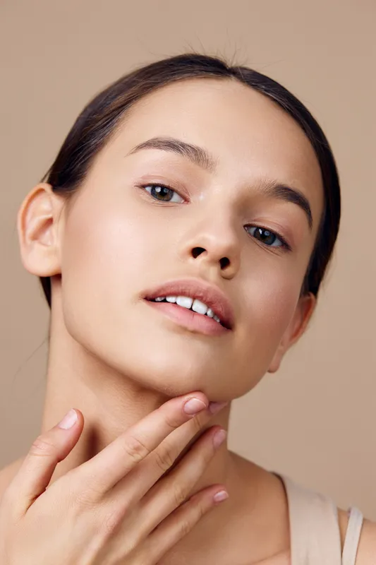 Portrait of a young woman with clear skin and natural makeup, showcasing beauty and confidence against a soft beige background
