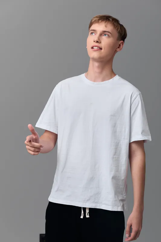 Young man in a white tee points upward in a clean studio, conveying curiosity and modern style, casual mood, and creative thinking for lifestyle, education, and design themes