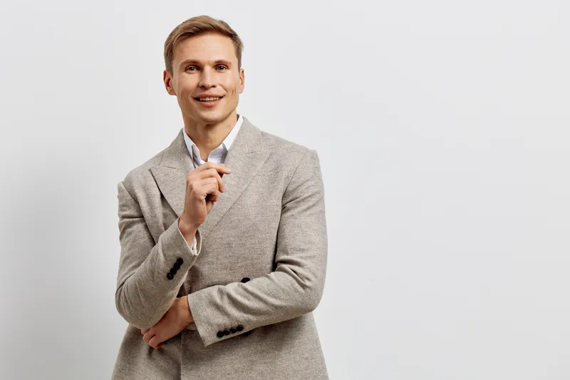Smiling man in light grey blazer posing confidently on plain white background. Modern professional look, casual style, positive expression, studio portrait, business, people lifestyle concept, cheerfu