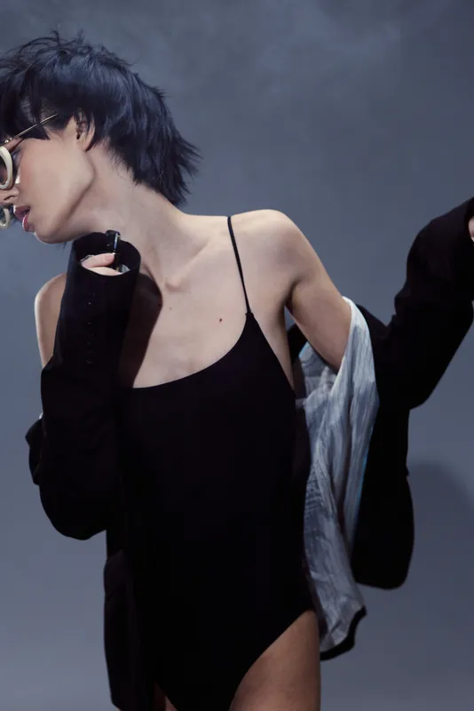 Stylish woman in black dress and glasses posing with off-shoulder jacket, modern fashion look, moody lighting, cool tone
