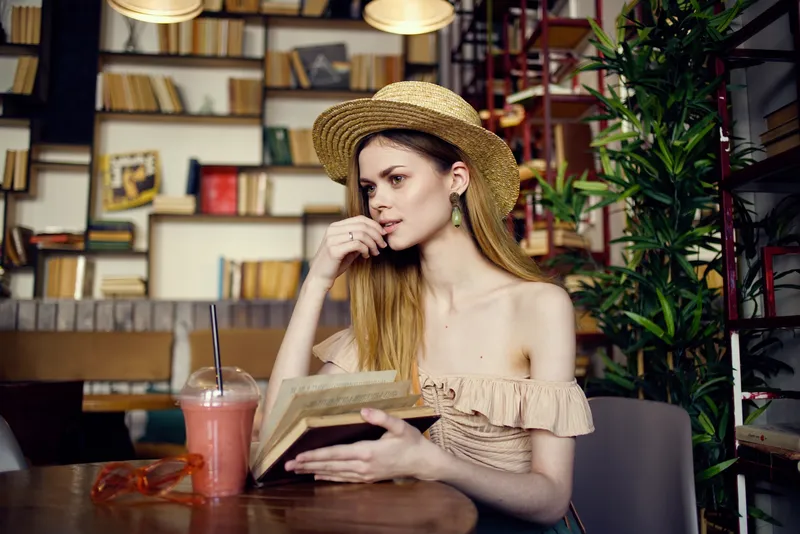 Женщина читает книгу и отдыхает в кафе с напитком, наслаждаясь досугом