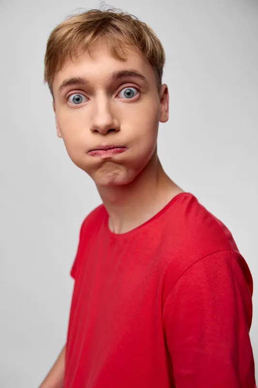Boy with a red shirt displays a surprised, puzzled facial expression, captured in a studio setting to convey curiosity, humor, and spontaneous reaction for youth lifestyle or emotion themes