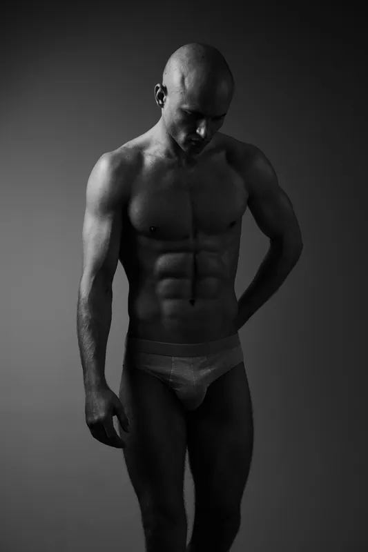 Black and white portrait of a muscular man, showcasing strength and expression, conveying emotion through body language and posture in a minimalistic style.