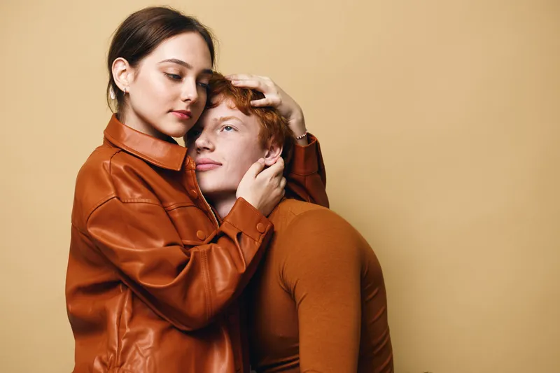 Couple, woman and man embracing with closed eyes in warm tones. Female with calm expression in leather jacket holds male closely, expressing love and comfort in studio setting.