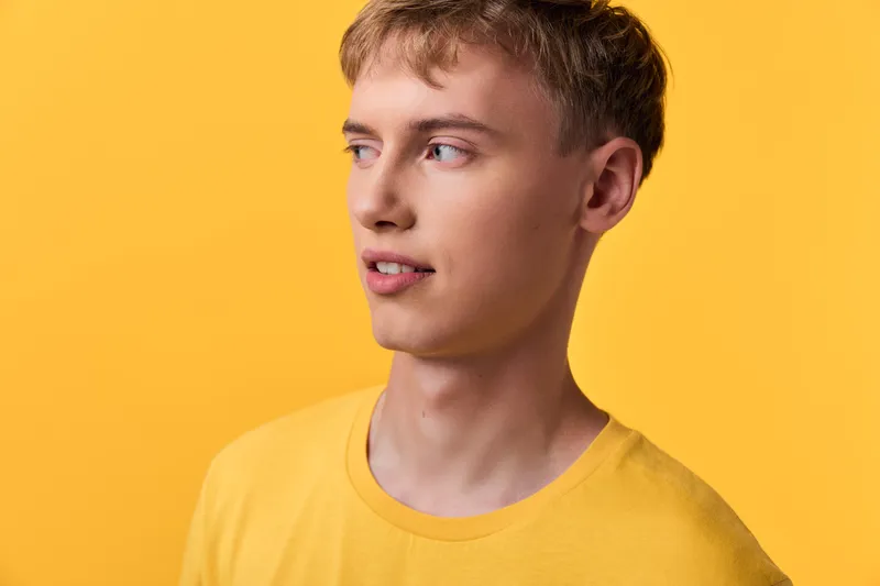 Young man in a yellow shirt against a bright yellow backdrop, studio lighting, casual mood, clean composition for fashion, lifestyle and product promotion in stock.
