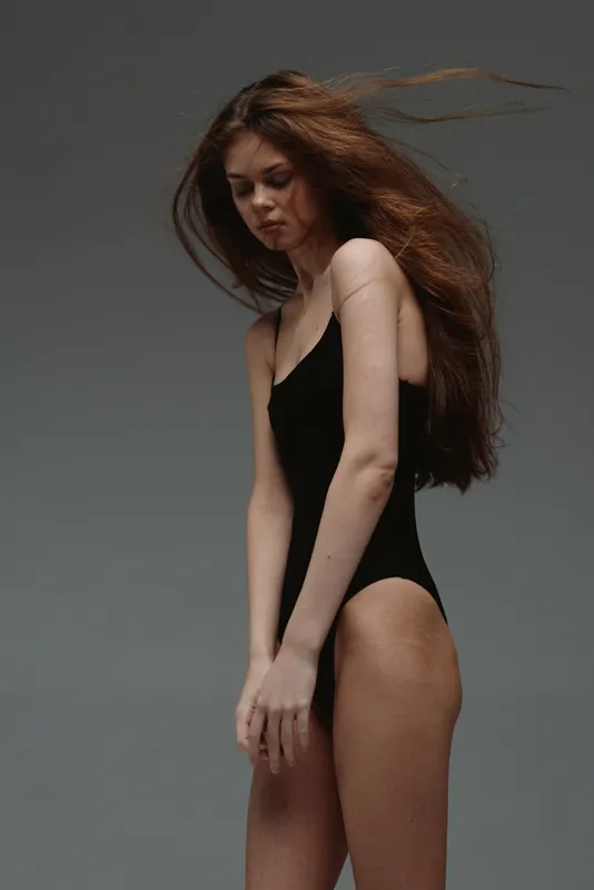 young woman with long red hair in black bodysuit in studio with neutral background