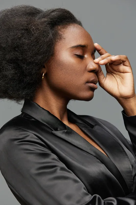 Calm and reflective portrait of a Black woman in a silk black blouse, eyes closed, expressing serenity and introspection against a neutral grey background