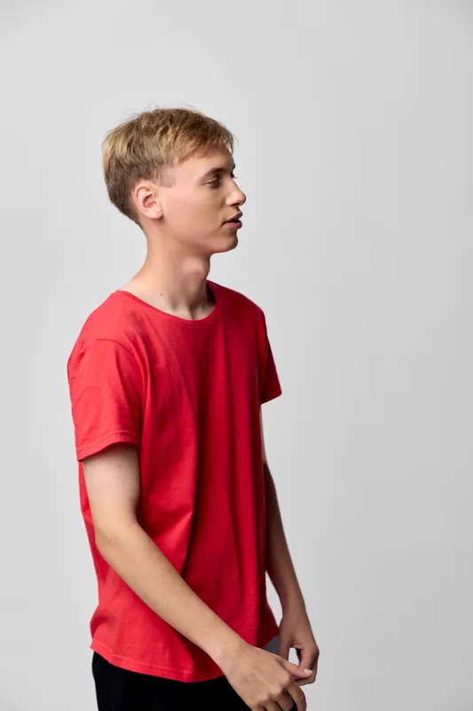 Boy in a red t shirt stands in side profile against a neutral gray backdrop, a casual youth image suited for lifestyle, fashion, and modern everyday photography.