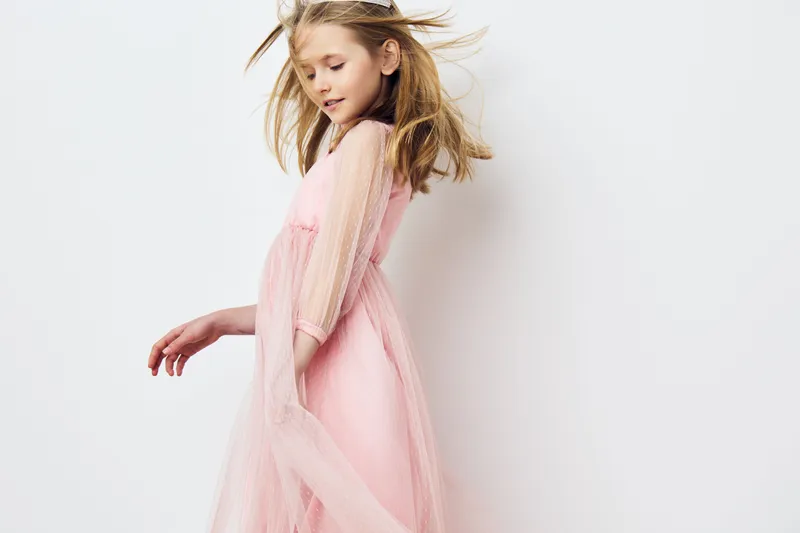 Young girl in a pink tulle dress joyfully dancing against a white backdrop, embodying innocence and playfulness in a whimsical spring setting