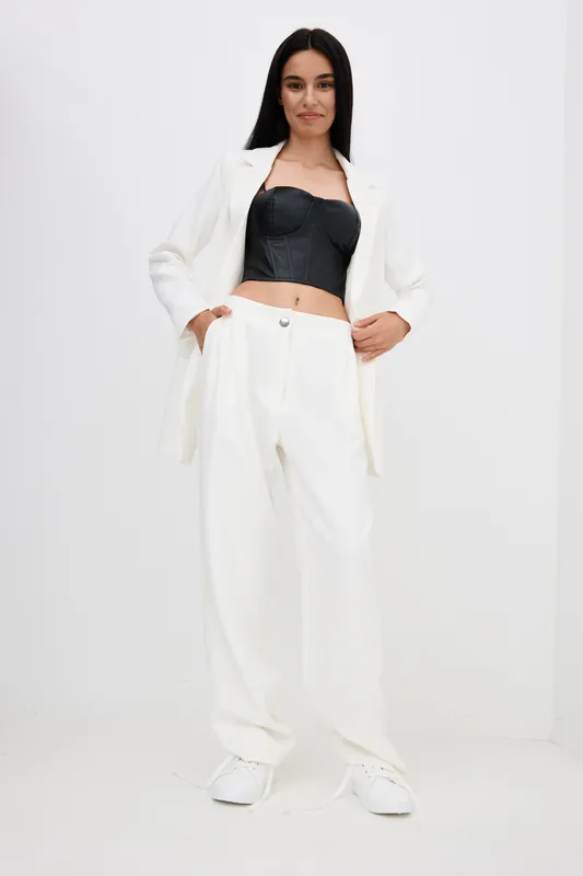 Stylish woman wearing a black corset top and white suit with wide-leg pants, posing confidently against a plain white background in a modern fashion look.