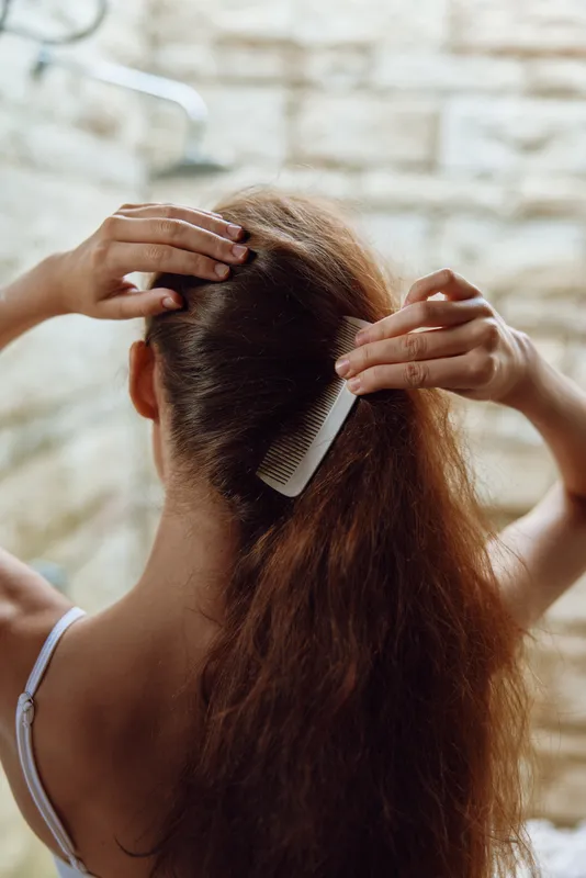Woman combing long thick hair in a bright bathroom with natural light, showing careful grooming and hair care routine.