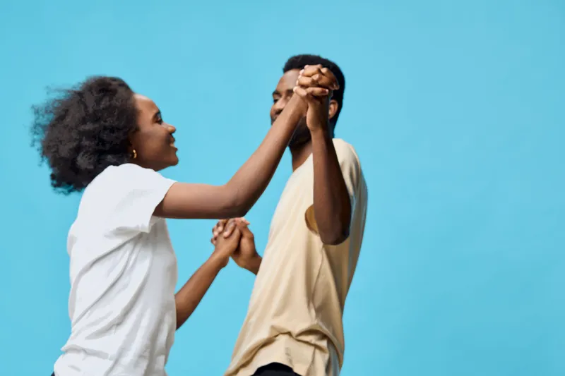 Happy African couple dancing together against a bright blue background, showcasing joy and connection through their clothing and expressions