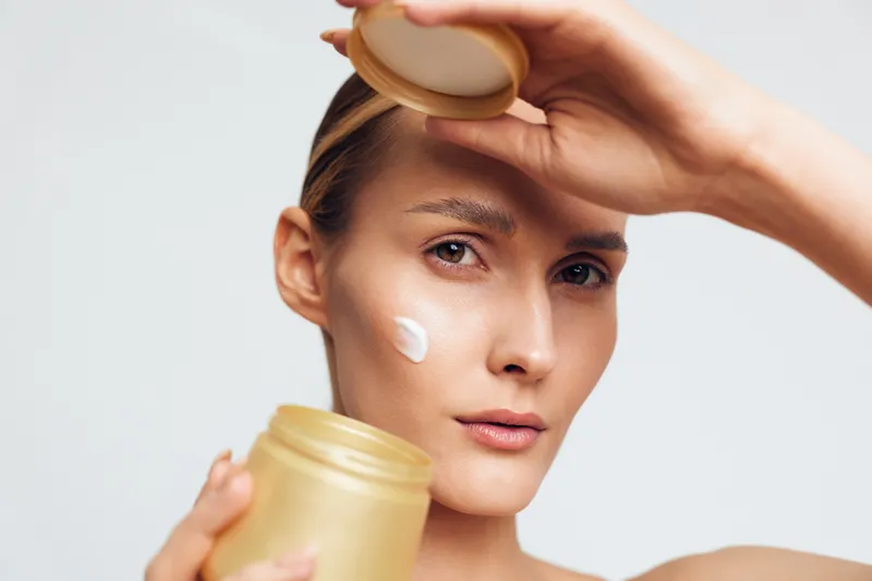 Young woman applies cream from a jar on her forehead in a close up skincare moment, soft lighting highlighting smooth skin and a calm focused expression