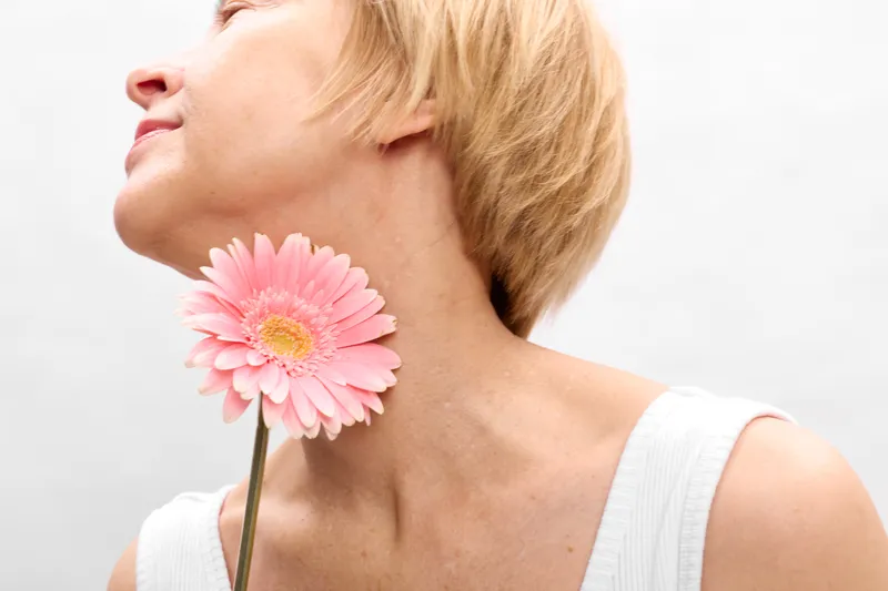 Woman holds pink gerbera flower at her neck eyes closed relaxed expression on a bright minimal background beauty and spring tenderness concept for skincare and self care portrait