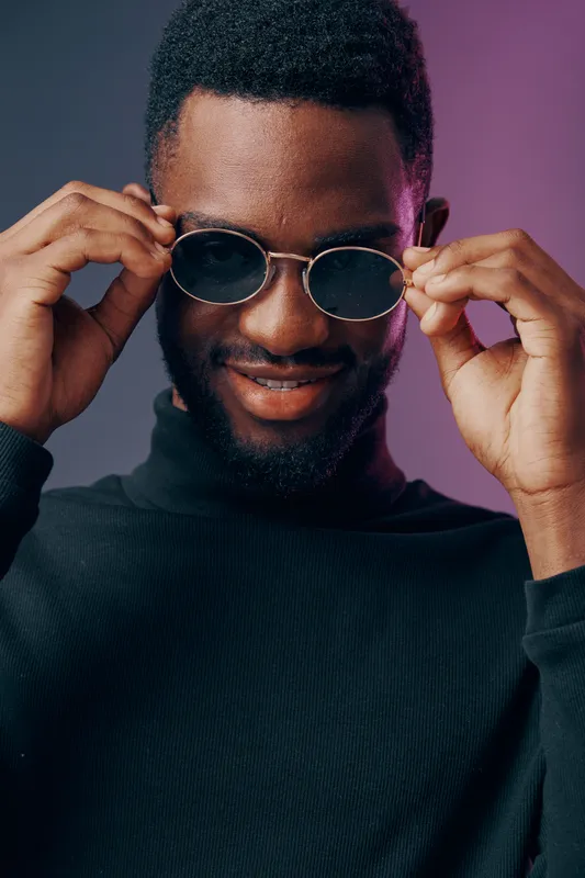 Stylish young man with sunglasses, showcasing confidence and modern fashion against a vibrant purple and grey background, perfect for lifestyle and fashion concepts