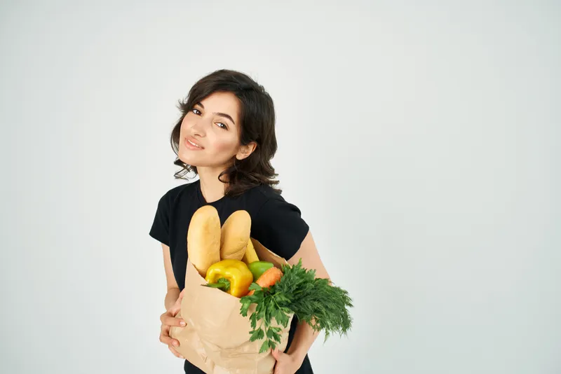 Женщина с бумажным пакетом продуктов в руках доставляет овощи для здорового питания