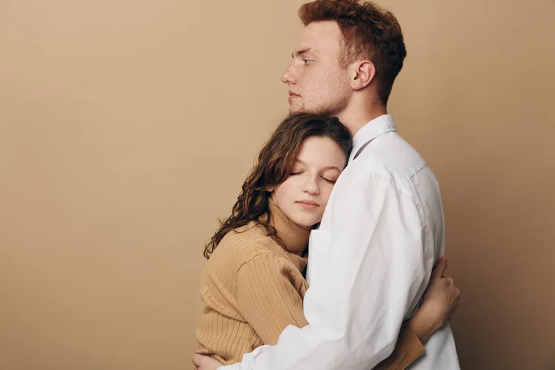 Young couple embraces tenderly with eyes closed against beige background. Intimate moment of affection and comfort, expressing love, trust, and emotional connection between partners.