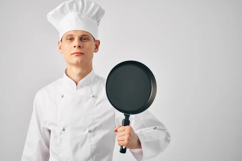 Мужчина в авторской форме держит сковороду в руках, готовит, кухонный предмет