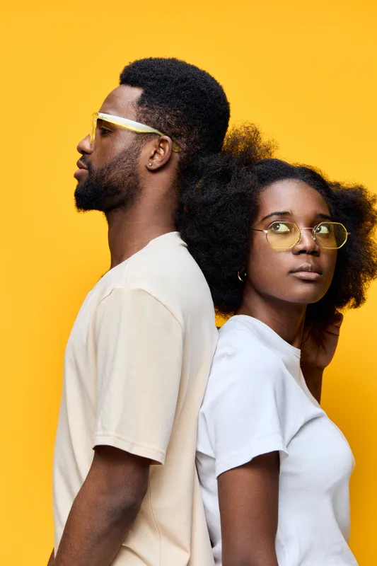 Young African couple posing back to back with stylish glasses against a bright yellow background, showcasing modern fashion and confidence