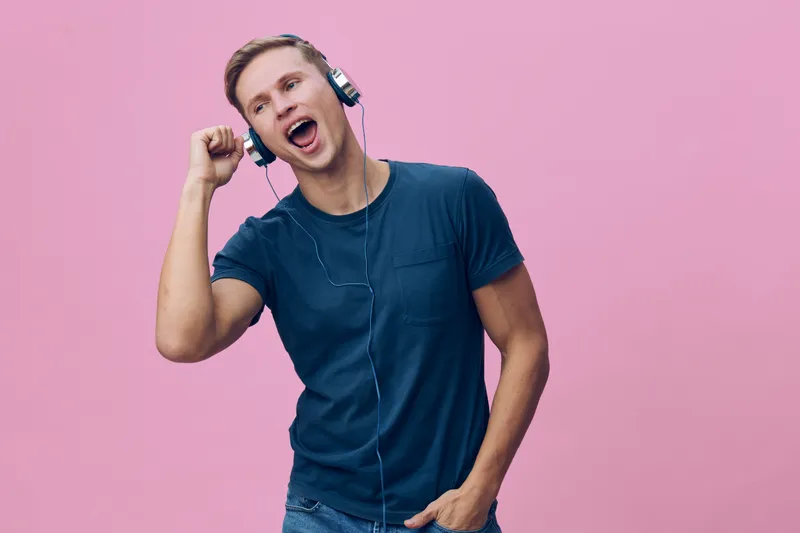 excited happy young man wearing headphones and casual t-shirt listening to music isolated on pink background digital detox lifestyle concept