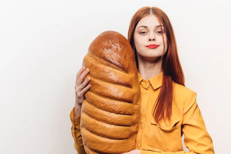 Портрет счастливой женщины с батоном на светлом фоне, в жёлтой рубашке и с макияжем