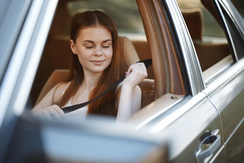 Young woman fastening her seatbelt in a car, smiling, with natural light illuminating her features, evoking a sense of safety and comfort.