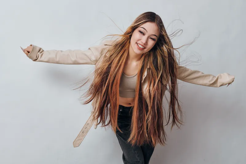 Young woman with long hair and dreadlocks posing with arms outstretched smiling and wearing casual clothes on plain light background in studio photo session.
