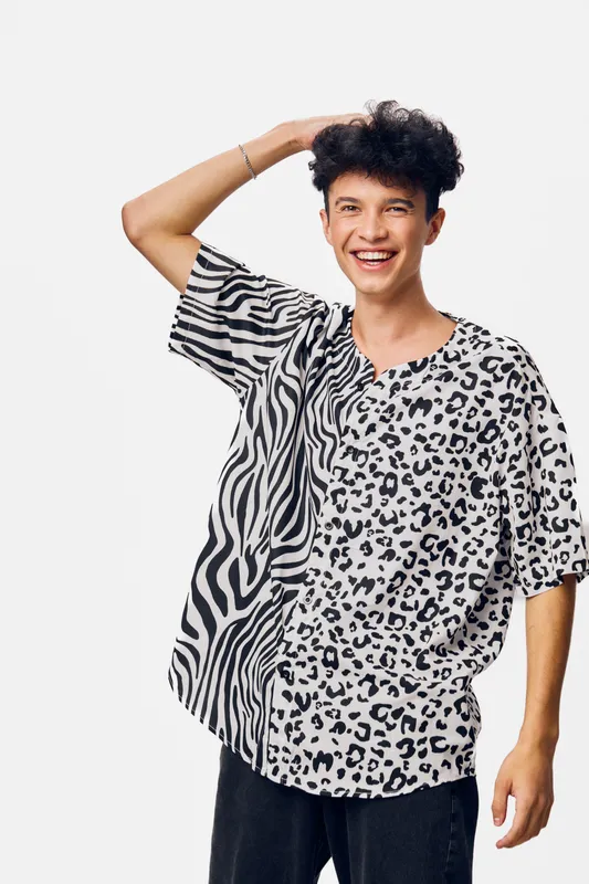 Smiling man in animal print shirt with mixed zebra and leopard patterns posing joyfully against white background in casual style, black hair, and relaxed expression.