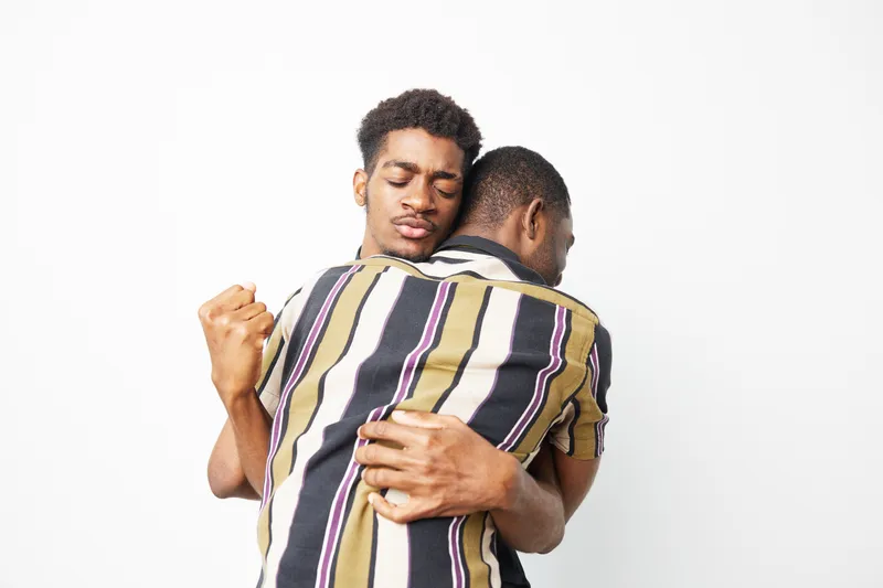 Two black men embracing each other, showcasing a powerful moment of connection and support. The intimate setting highlights their bond and shared emotions.